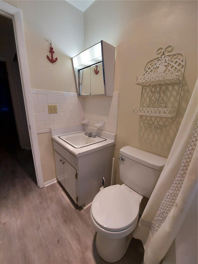 bathroom with hardwood / wood-style floors, tile walls, toilet, vanity, and a shower with curtain