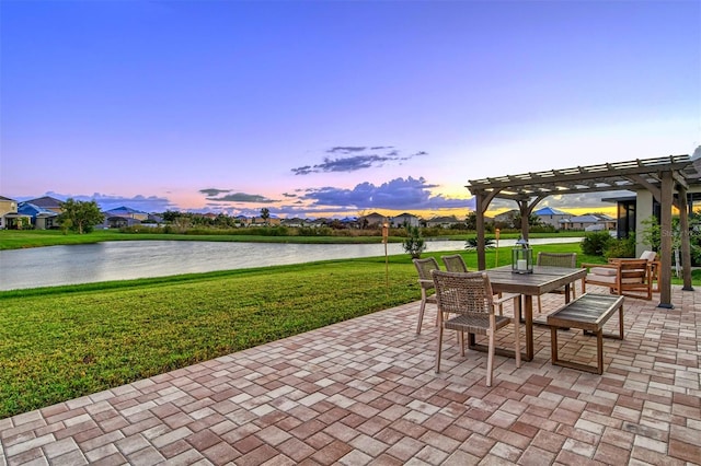 patio terrace at dusk featuring a lawn, a water view, and a pergola