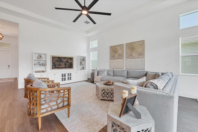 living room featuring ceiling fan, a healthy amount of sunlight, a towering ceiling, and hardwood / wood-style floors