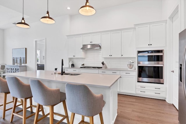 kitchen featuring sink, a kitchen island with sink, decorative light fixtures, and white cabinetry