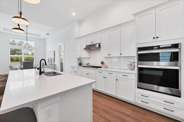 kitchen featuring stainless steel appliances, sink, light wood-type flooring, and hanging light fixtures