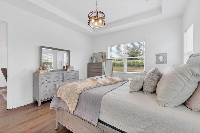 bedroom with light hardwood / wood-style flooring, a notable chandelier, and a raised ceiling