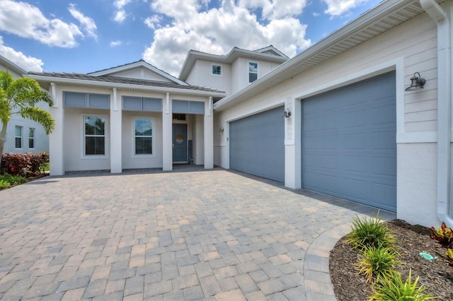 view of front of home with decorative driveway, an attached garage, and stucco siding