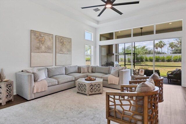 living area with visible vents, ceiling fan, a towering ceiling, and wood finished floors