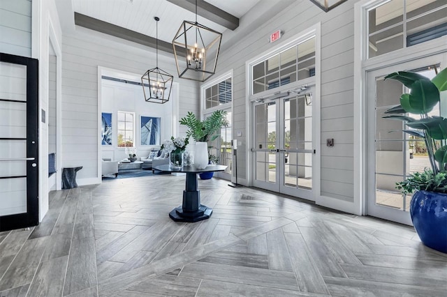 foyer featuring wooden walls, a high ceiling, french doors, beamed ceiling, and an inviting chandelier