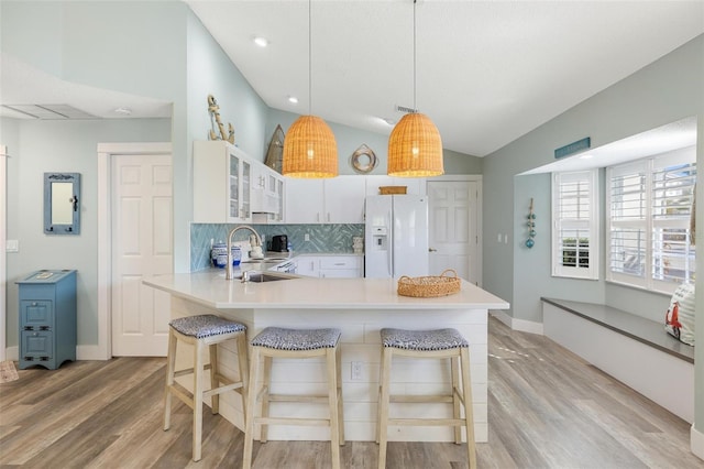 kitchen with white cabinets, white refrigerator with ice dispenser, light hardwood / wood-style floors, and kitchen peninsula