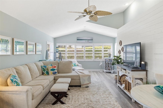 living room with lofted ceiling, hardwood / wood-style floors, wooden walls, and ceiling fan