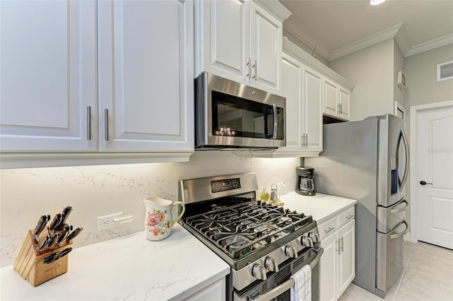 kitchen with light tile patterned flooring, white cabinetry, crown molding, light stone counters, and appliances with stainless steel finishes