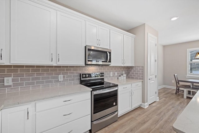 kitchen with white cabinets, backsplash, light wood-type flooring, stainless steel appliances, and light stone counters