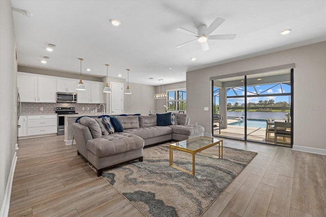 living room featuring a water view, light wood-type flooring, and ceiling fan