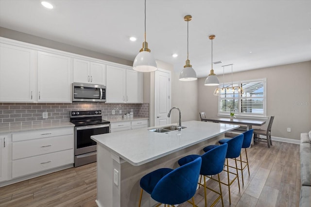 kitchen with appliances with stainless steel finishes, light hardwood / wood-style flooring, white cabinets, and a kitchen island with sink