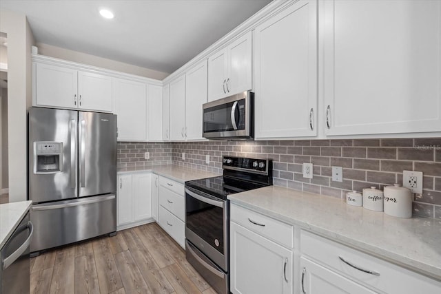 kitchen with white cabinets, backsplash, appliances with stainless steel finishes, light wood-type flooring, and light stone counters