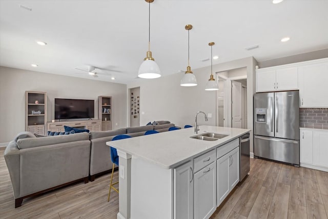 kitchen with appliances with stainless steel finishes, hanging light fixtures, a kitchen island with sink, and white cabinets