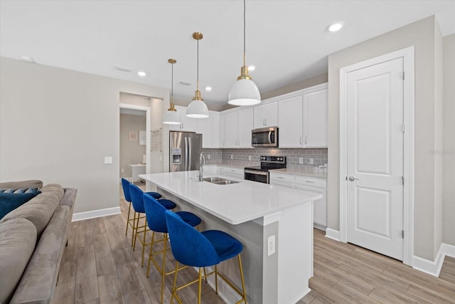 kitchen with pendant lighting, white cabinets, light hardwood / wood-style flooring, and stainless steel appliances