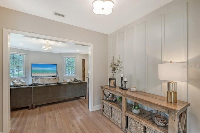 hall with light hardwood / wood-style flooring, ornamental molding, and a healthy amount of sunlight