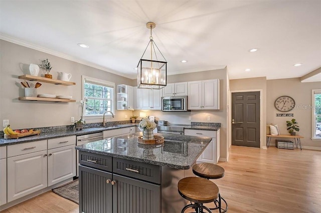 kitchen with hanging light fixtures, appliances with stainless steel finishes, white cabinetry, light hardwood / wood-style floors, and a center island