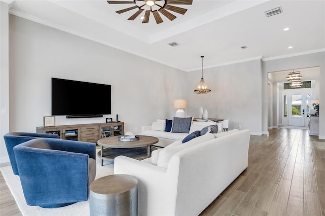 living room with light hardwood / wood-style floors, crown molding, and ceiling fan with notable chandelier