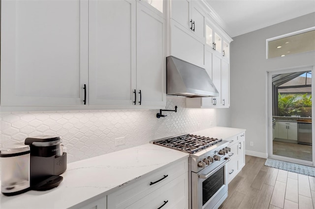 kitchen with white cabinets, exhaust hood, light stone counters, light hardwood / wood-style floors, and stainless steel appliances