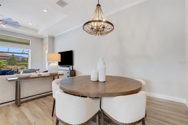 dining space featuring an inviting chandelier, ornamental molding, a tray ceiling, and light wood-type flooring