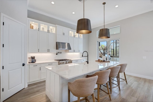 kitchen featuring extractor fan, hanging light fixtures, a center island with sink, white cabinets, and light hardwood / wood-style floors