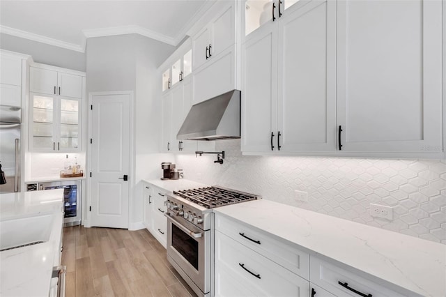 kitchen with premium appliances, light stone countertops, light wood-type flooring, wall chimney exhaust hood, and white cabinets