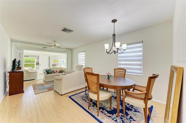 dining room with a textured ceiling, light wood-type flooring, and ceiling fan with notable chandelier