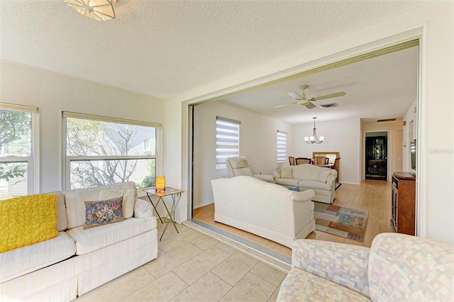 tiled living room with a textured ceiling and ceiling fan with notable chandelier