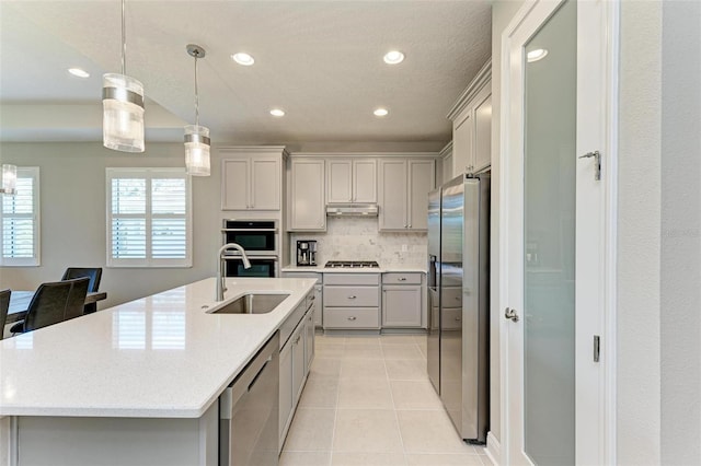 kitchen with appliances with stainless steel finishes, sink, pendant lighting, and an island with sink