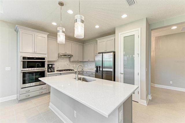 kitchen featuring appliances with stainless steel finishes, sink, hanging light fixtures, decorative backsplash, and a center island with sink