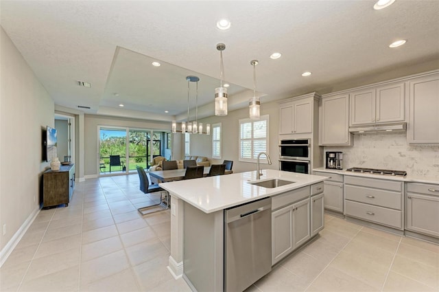 kitchen with appliances with stainless steel finishes, sink, gray cabinets, and an island with sink