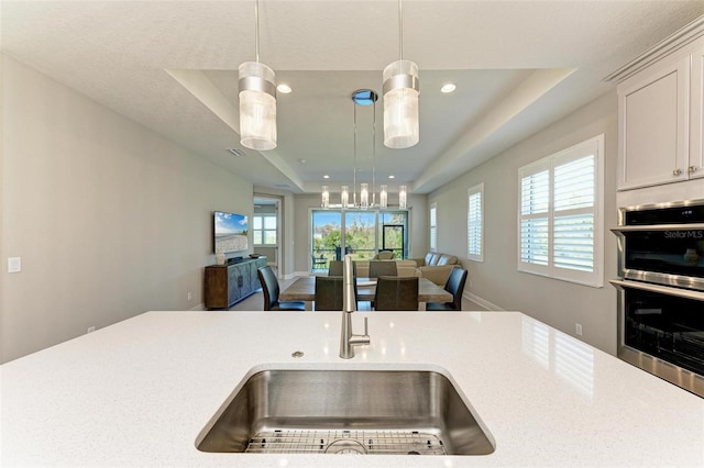 kitchen featuring a raised ceiling, sink, stainless steel double oven, and hanging light fixtures