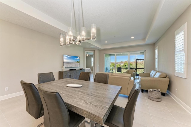 dining space featuring an inviting chandelier, a textured ceiling, light tile patterned floors, and a raised ceiling