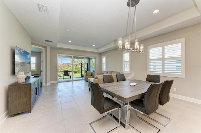 dining room with light tile patterned flooring, a tray ceiling, and an inviting chandelier