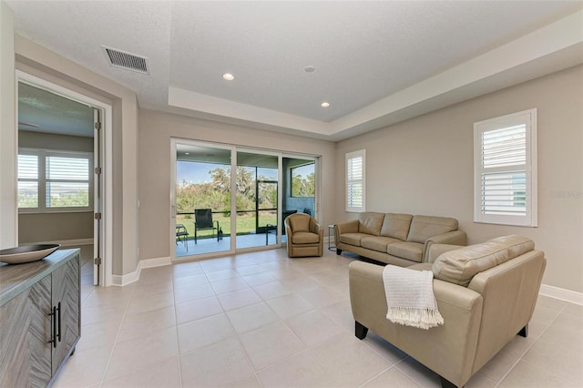 living room with a raised ceiling, a textured ceiling, and light tile patterned flooring