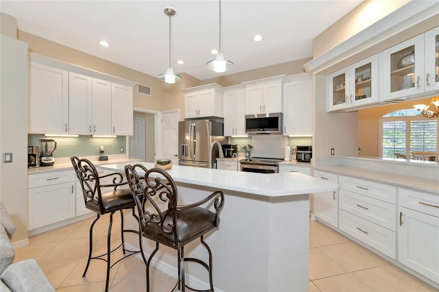 kitchen with appliances with stainless steel finishes, light tile patterned flooring, white cabinetry, and decorative light fixtures