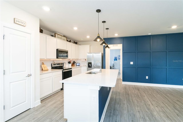 kitchen with an island with sink, stainless steel appliances, pendant lighting, light wood-type flooring, and white cabinets