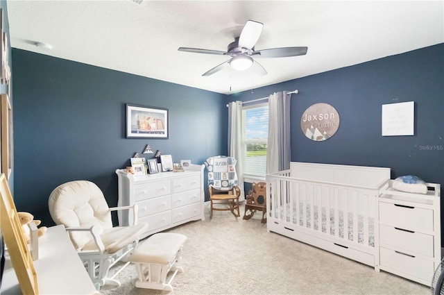 carpeted bedroom featuring ceiling fan and a crib