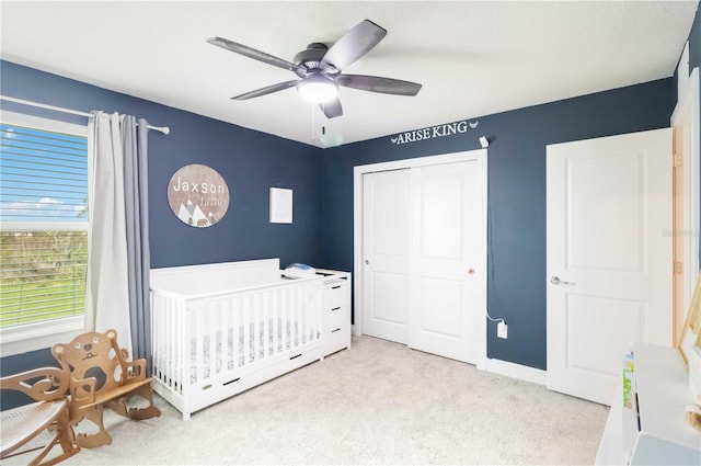 unfurnished bedroom featuring a closet, ceiling fan, light colored carpet, and a nursery area