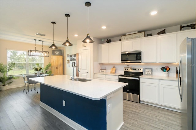 kitchen featuring sink, white cabinetry, stainless steel appliances, pendant lighting, and a center island with sink