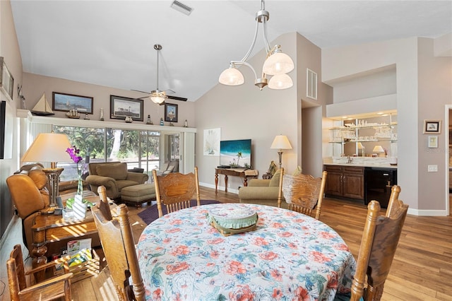 dining space featuring sink, high vaulted ceiling, ceiling fan with notable chandelier, and light wood-type flooring