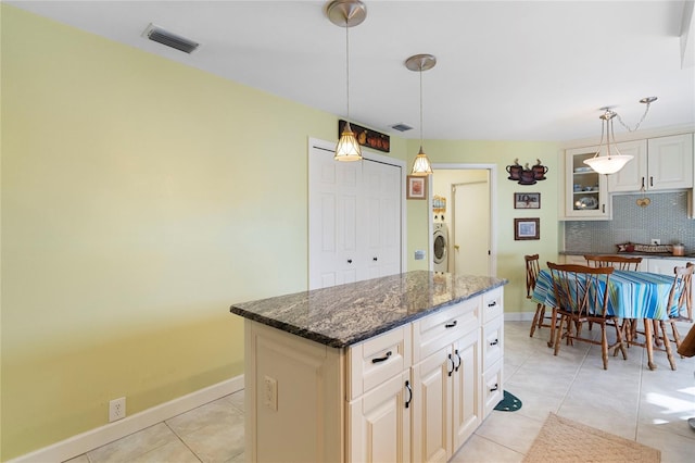 kitchen with tasteful backsplash, light tile patterned floors, a kitchen island, dark stone counters, and pendant lighting