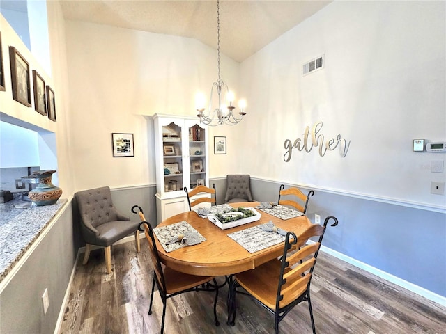 dining area with a notable chandelier, dark wood-type flooring, and vaulted ceiling