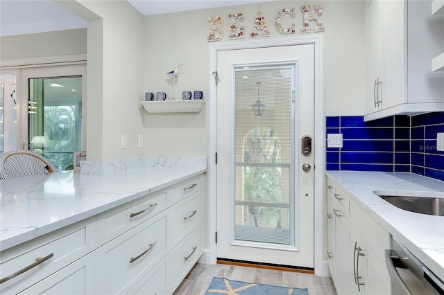 kitchen with white cabinetry, dishwasher, light stone counters, and a wealth of natural light