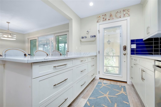 kitchen with a wealth of natural light, white cabinetry, decorative light fixtures, and light hardwood / wood-style floors