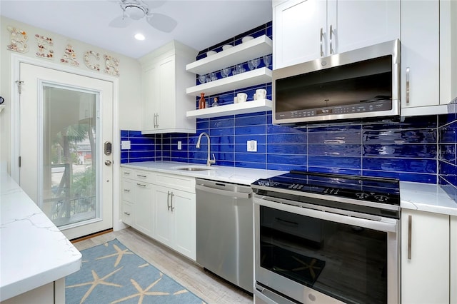 kitchen featuring white cabinets, appliances with stainless steel finishes, light stone countertops, light hardwood / wood-style floors, and sink