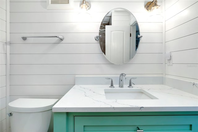 bathroom with vanity, wood walls, and toilet