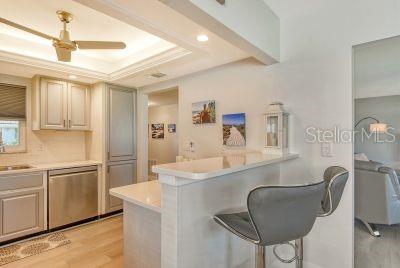 kitchen featuring kitchen peninsula, a tray ceiling, a kitchen bar, stainless steel dishwasher, and light hardwood / wood-style floors