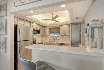 kitchen with sink, a raised ceiling, kitchen peninsula, ceiling fan, and stainless steel appliances