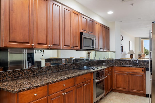 kitchen featuring appliances with stainless steel finishes, light tile patterned flooring, sink, and dark stone counters