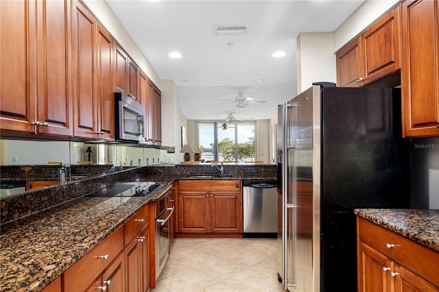 kitchen with ceiling fan, appliances with stainless steel finishes, light tile patterned floors, dark stone counters, and sink